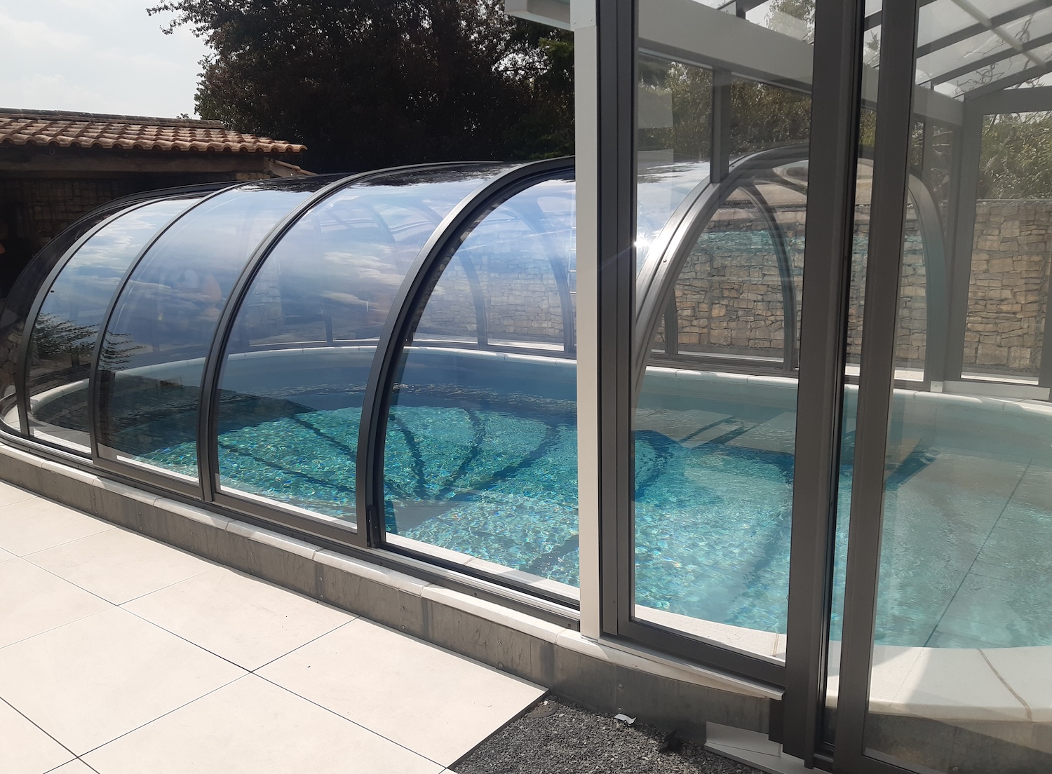 20260731_132711 Seitliche Ansicht einer geschlossenen Poolüberdachung mit gebogenen Glaselementen und Verbindung zur Terrasse.