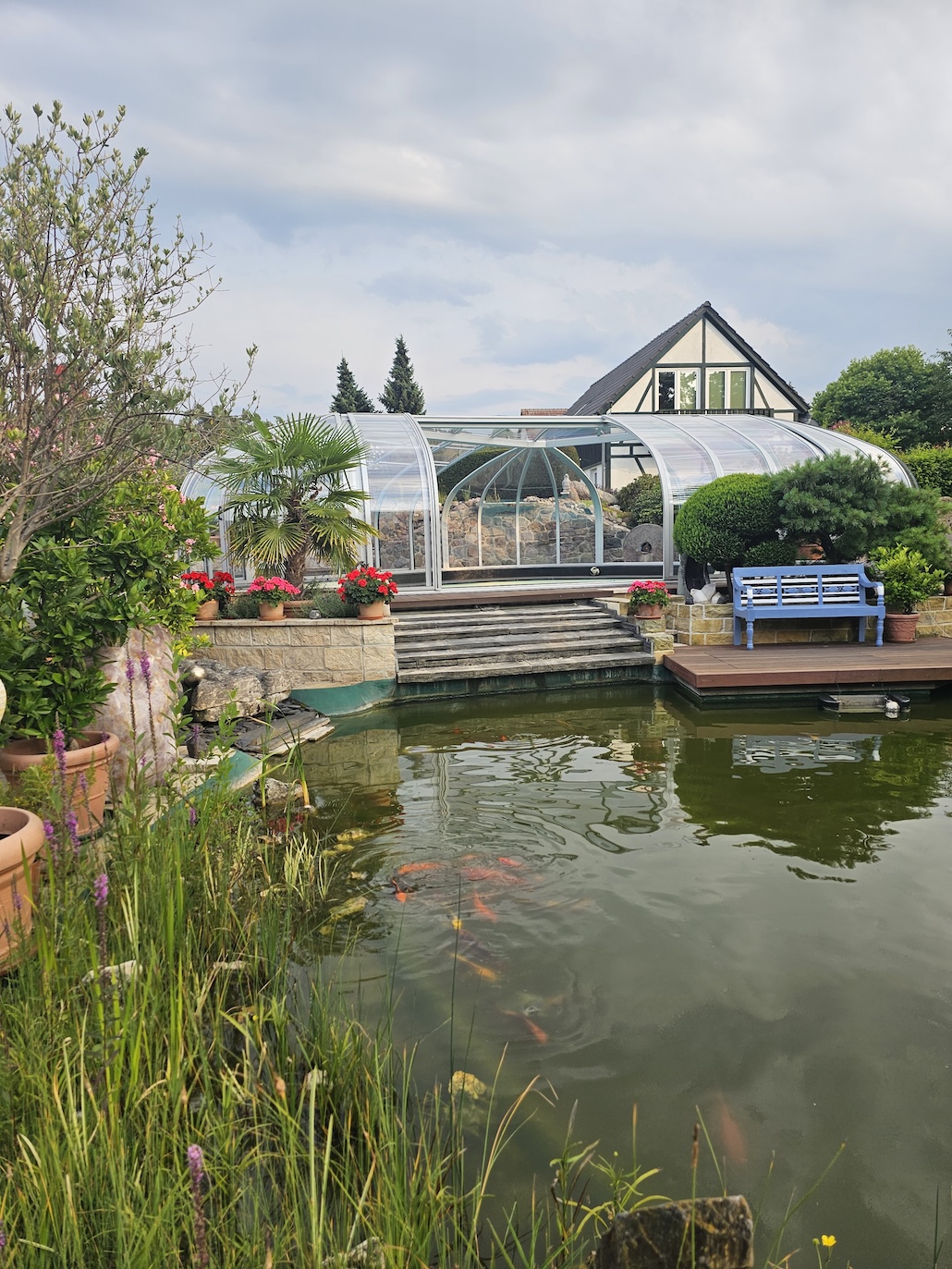 20260731_185324 Begehbare Poolüberdachung in einem gepflegten Garten mit Teich, Steintreppe und Sitzbank