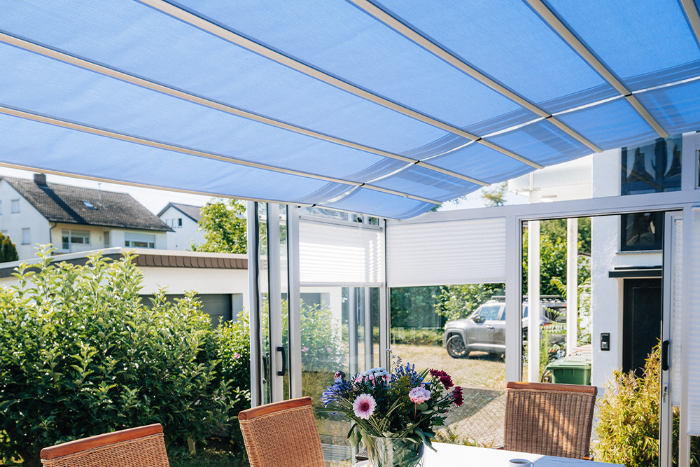 A side view beneath the blue-shaded roof surfaces of the patio canopy with white frame profiles.
