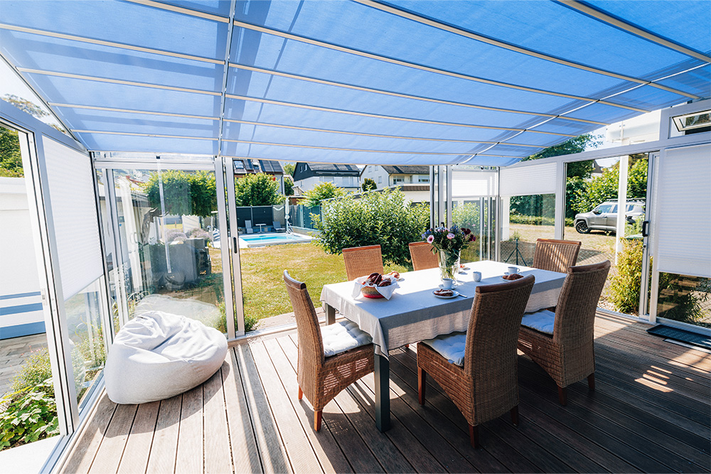 A dining table with chairs under the blue-shaded patio canopy, overlooking the garden.