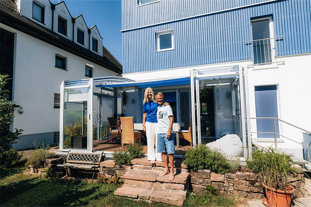 Two customers standing in front of their TOPAS Solar Veranda patio cover with white profiles attached to their home.