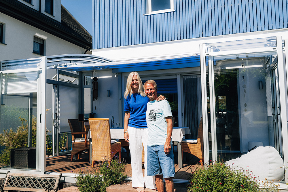 Two customers standing in front of their TOPAS Solar Veranda patio cover with white profiles attached to their home.